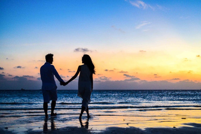Muž a žena držiaci sa za ruky sa prechádzajú po pláži.jpg