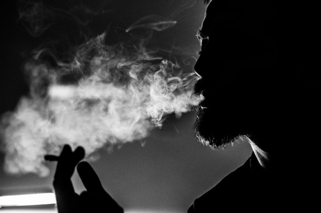 Muž s cigaretou v ruke vyfukuje dym z úst.jpg